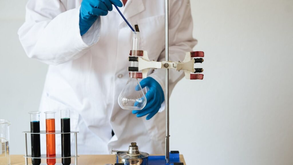 Gloved hands inserting a pipette into a laboratory flask